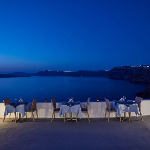  
Santorini View Hotel restaurant terrace with table seats and caldera view, at evening