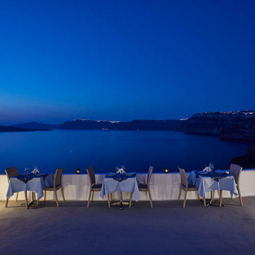  
Santorini View Hotel restaurant terrace with table seats and caldera view, at evening
