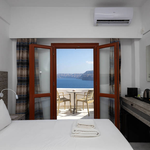 Standard Room interior with double bed and balcony doors opening to a panoramic caldera and sea view
