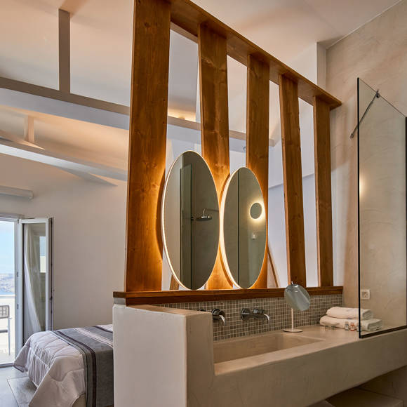 Elegant open-plan suite with illuminated mirrors, natural wood accents and sea-view balcony