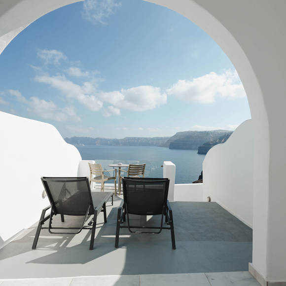Terrace with sun loungers and sea-view framed by a white arch overlooking the Santorini caldera