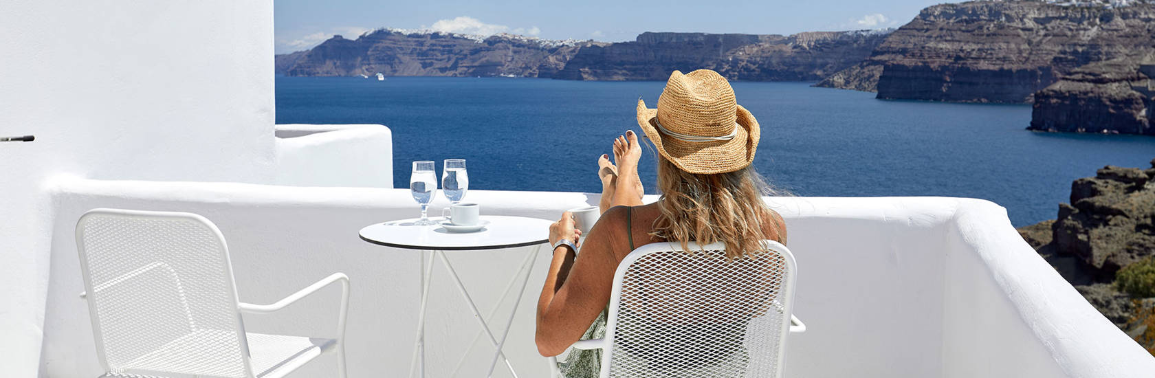 
Santorini View Hotel woman with a hat seating at a sea view balcony enjoying the view and drinking coffee