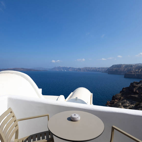 Balcony of the Standard Room with table and chairs overlooking the stunning Santorini caldera and Aegean Sea