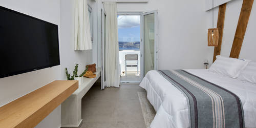
Santorini View Hotel double bed with white and grey linen, wooden decoration, white curtains and balcony with sea view