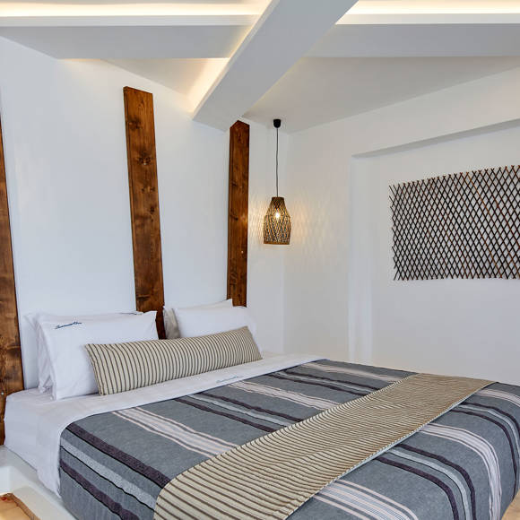 Stylish Suite bedroom at Santorini View Hotel with warm wooden accents, and elegant striped bedding