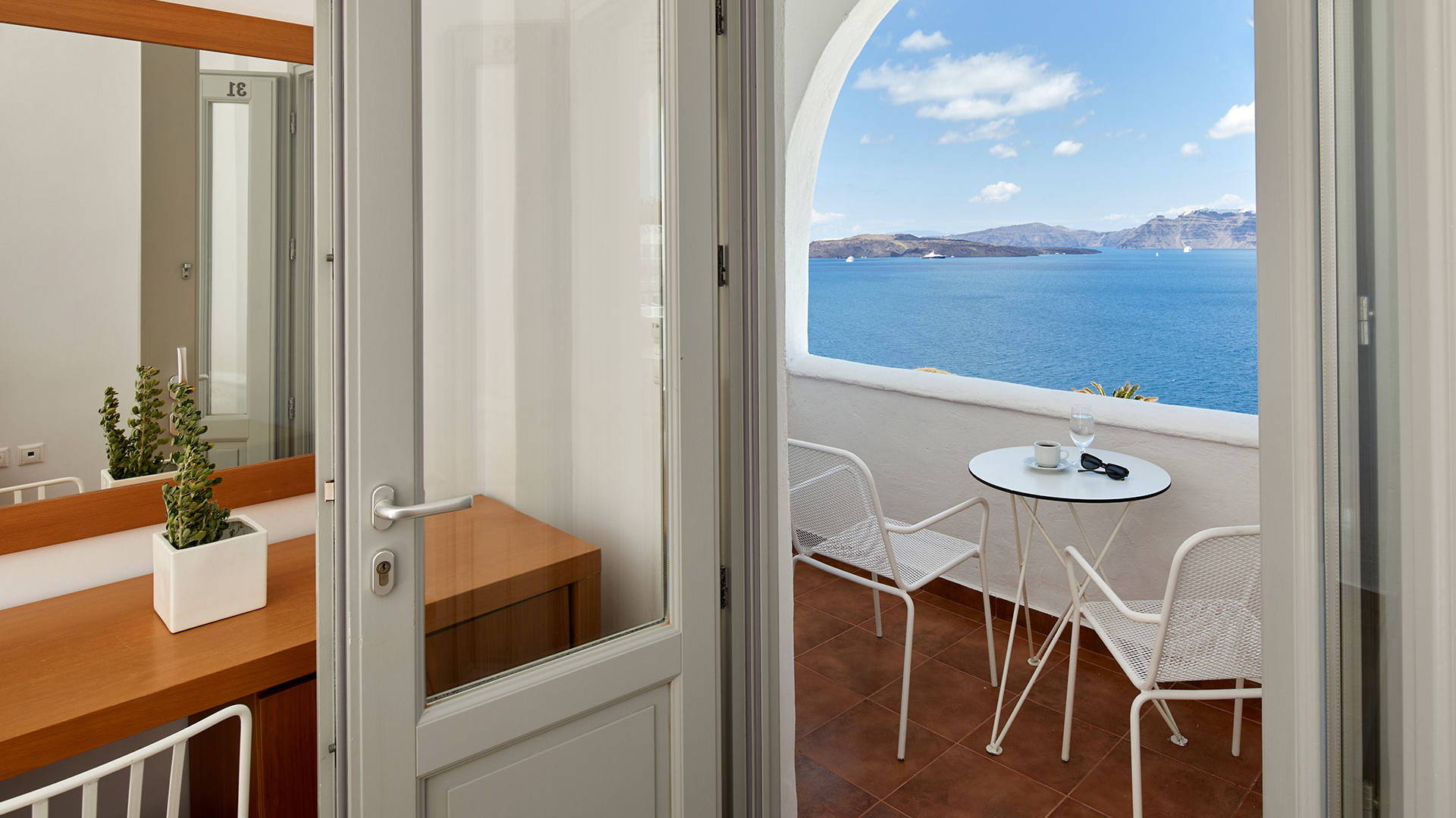 
Santorini View Hotel room with white door to sea view balcony with table and chairs