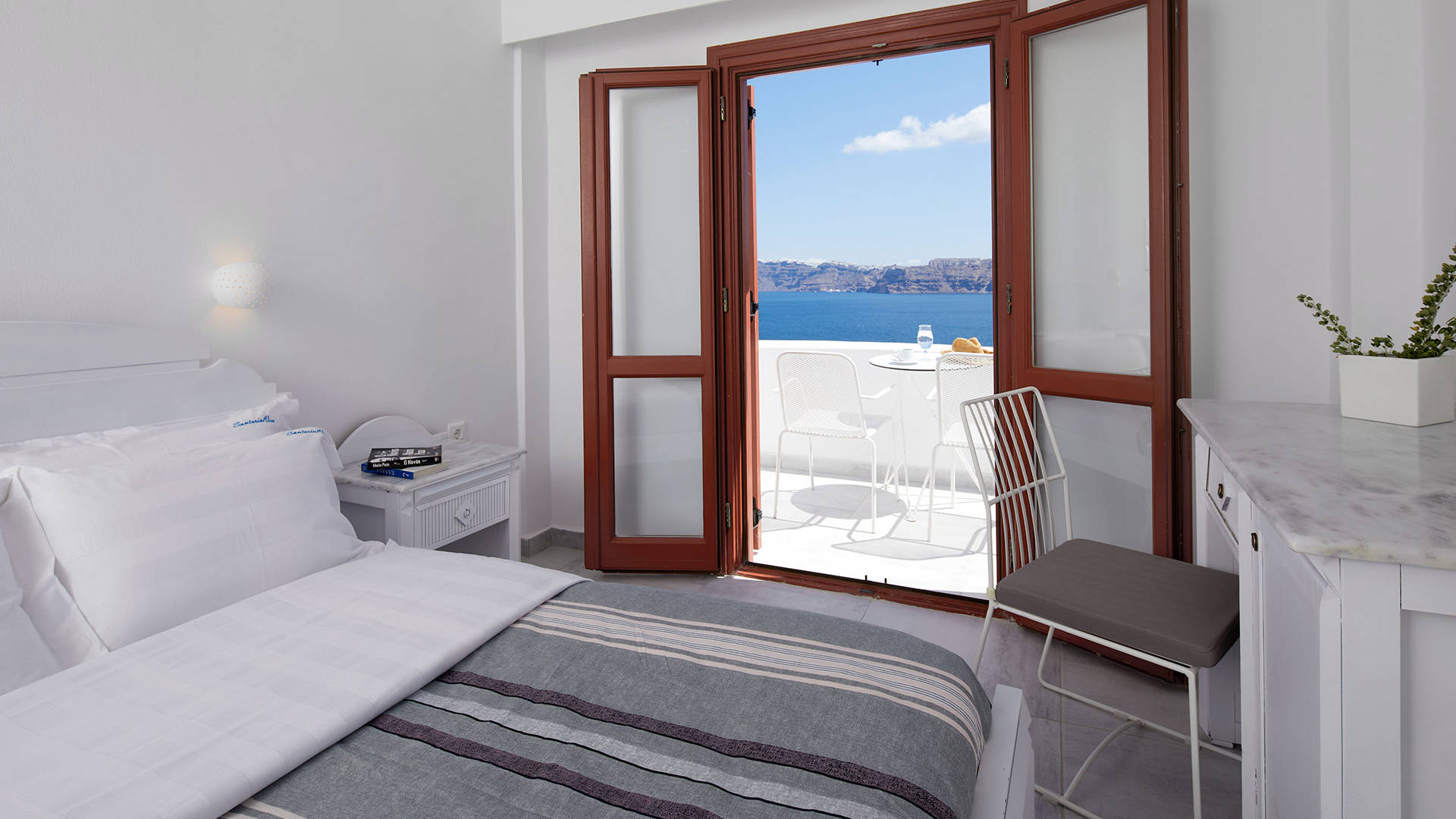 
Santorini View Hotel bedroom with king size bed with white and grey linen, and sea view balcony with white furniture