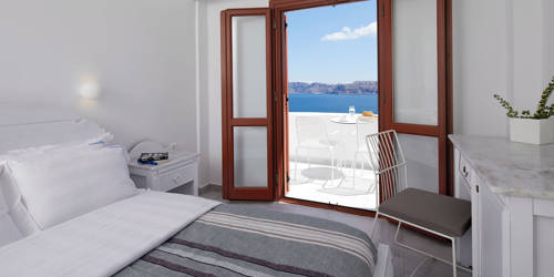 
Santorini View Hotel bedroom with king size bed with white and grey linen, and sea view balcony with white furniture