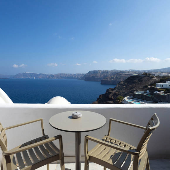 Private balcony of the Standard Room with table and chairs overlooking the caldera cliffs and Aegean sea
