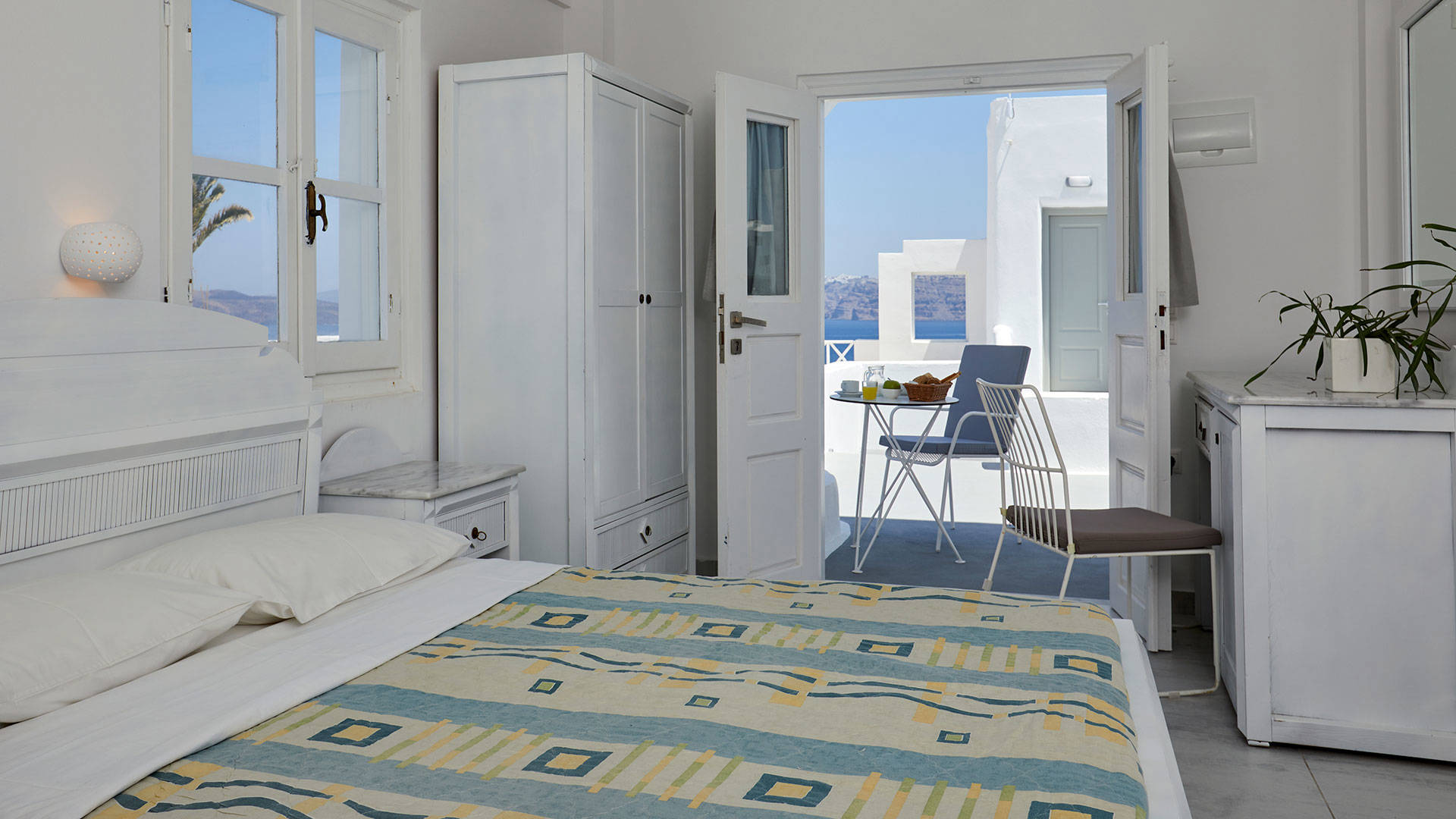 
Santorini View Hotel room with double bed, desk and mirror, and terrace with table seats for breakfast