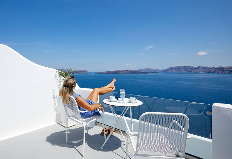 
Santorini View Hotel γυναίκα που κάθεται σε ένα μπαλκόνι με θέα στην καλντέρα και τη θάλασσα