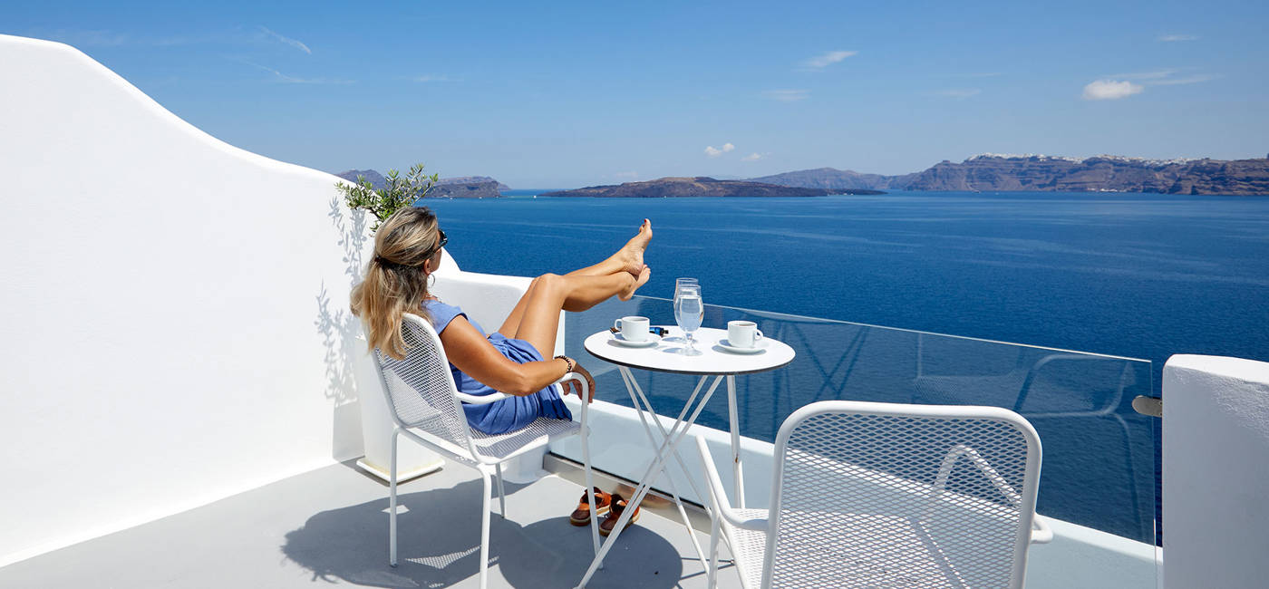 
Santorini View Hotel γυναίκα που κάθεται σε ένα μπαλκόνι με θέα στην καλντέρα και τη θάλασσα