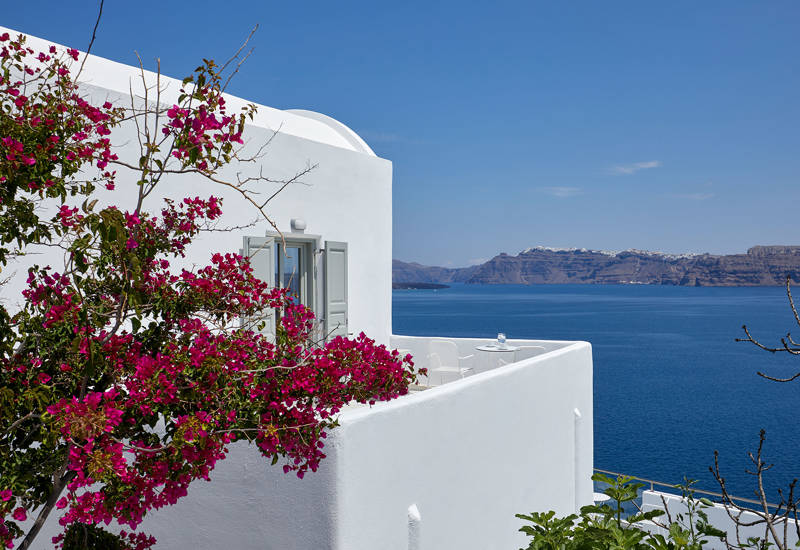 
Ξενοδοχείο με θέα στη Σαντορίνη με λευκό μπαλκόνι και λουλούδια βουκαμβίλιες, με απέραντη θέα στη θάλασσα και την καλντέρα