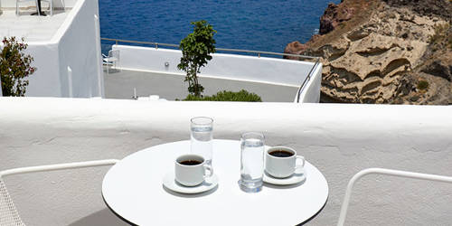 
Santorini View Hotel white table seats with greek coffee and glasses of water, at a sea view balcony