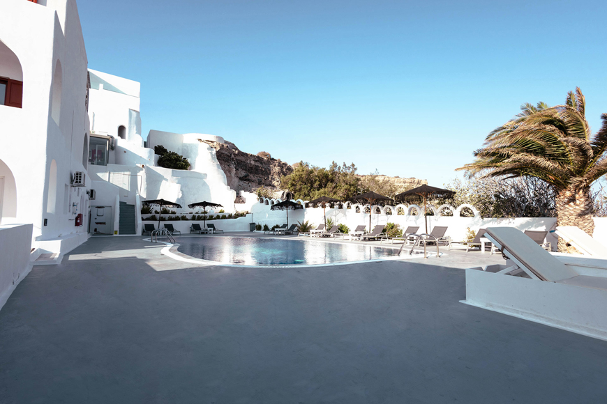 Stylish outdoor pool area of Santorini View Hotel with sunbeds, palm trees and whitewashed buildings 
