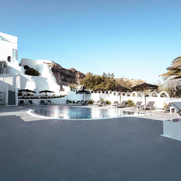 Stylish outdoor pool area of Santorini View Hotel with sunbeds, palm trees and whitewashed buildings 