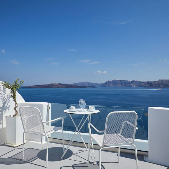 Private terrace of Deluxe Double room with white chairs and coffee table overlooking the deep blue Santorini caldera
