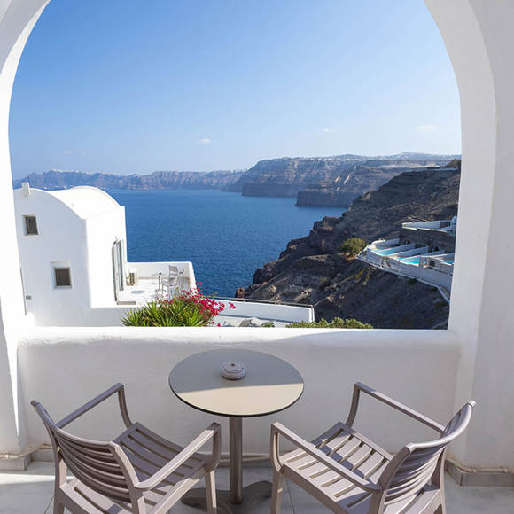 Balcony of the Superior Double room with arched view framing the caldera, blue sea and white Cycladic houses 