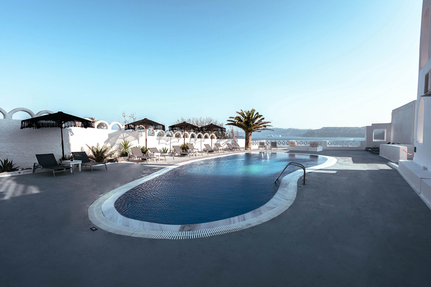 Outdoor swimming pool with sunbeds, palm tree, and caldera view at Santorini View Hotel