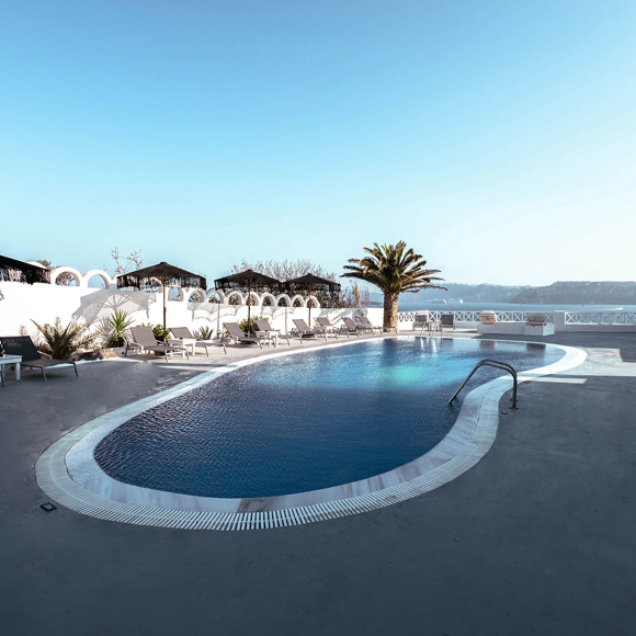 Outdoor swimming pool with sunbeds, palm tree, and caldera view at Santorini View Hotel