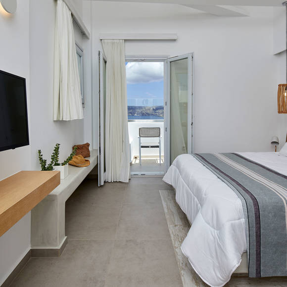 Elegant bedroom of Deluxe double room with natural wood accents, soft lighting and balcony overlooking the caldera