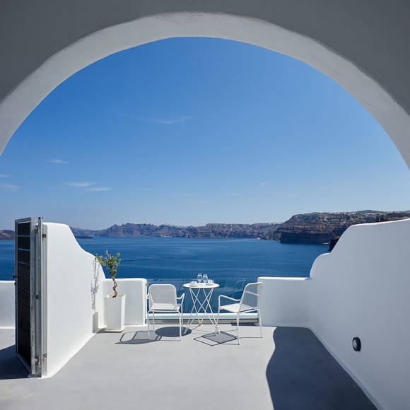 Deluxe Double room's big balcony in white colors with furniture and view at the Aegean sea and caldera
