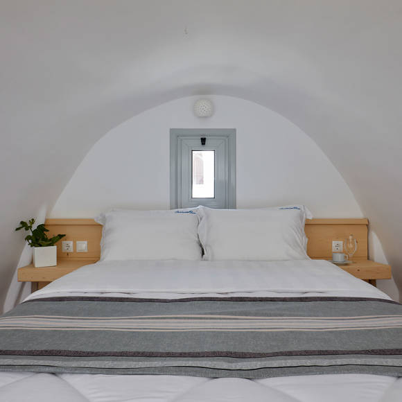 Cozy bedroom of the Junior Suite at Santorini View Hotel, with a vaulted ceiling, and a double bed with elegant linens