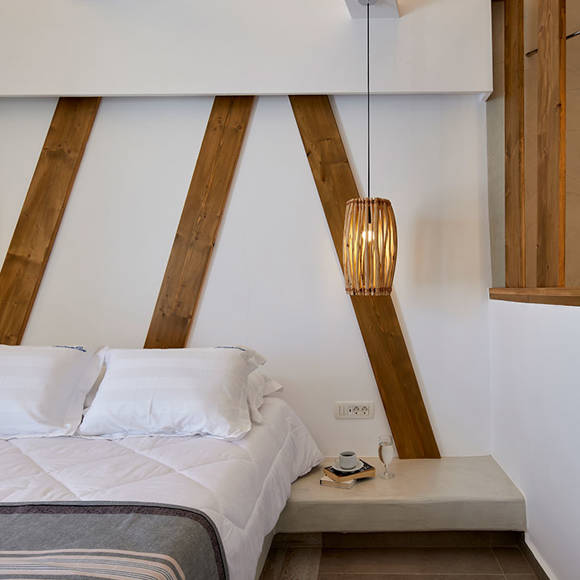 Cozy bed in Deluxe double room with wooden wall details, pendant lamp and a small bedside setup with coffee cup
