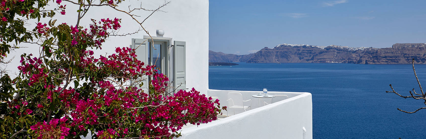 
Santorini View Hotel room with caldera sea view and white balcony with fuchsia bougainvillea undeer the blue sky